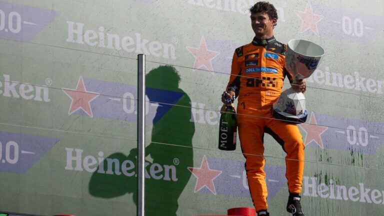 Lando Norris celebrating on the podium in McLaren kit with a trophy.
