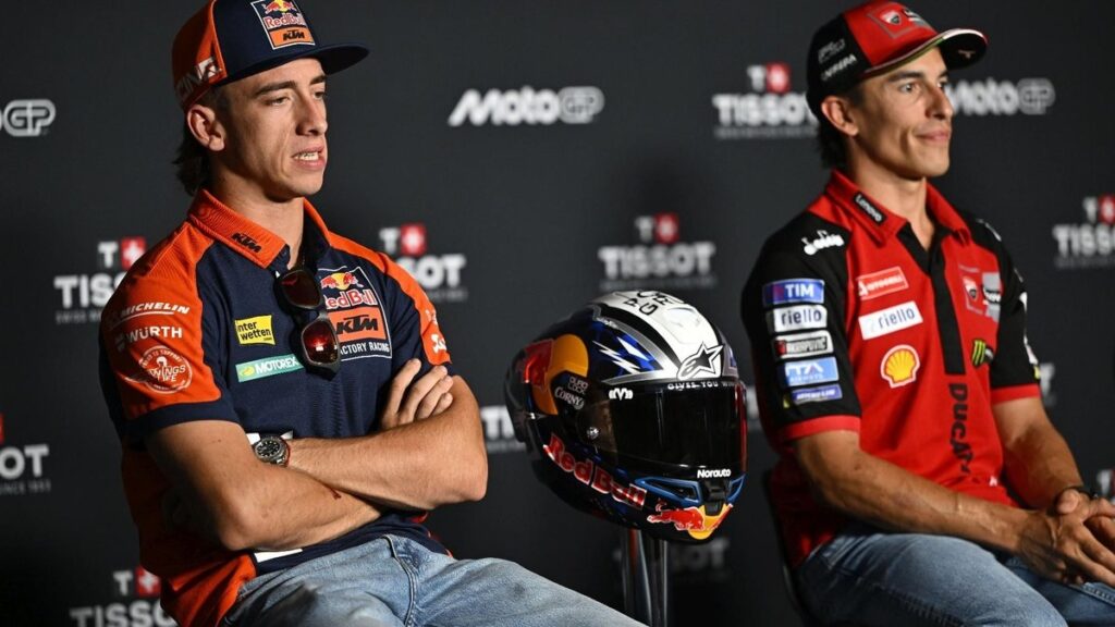 Pedro Acosta riding style: Pedro Acosta sitting in Red Bull KTM gear alongside Marc Márquez at a MotoGP press conference.