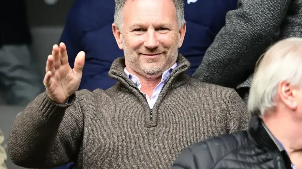 Christian Horner Ferrari: Christian Horner waving while sitting in the stands at a sports match.